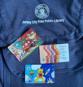 Variety of library card designs laying on a Jersey City Free Public Library backpack